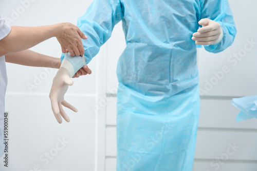 Close up of doctor in light-blue disposable medical suit putting gloves on photo