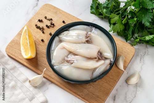 Fresh squid tubes in a bowl. Small calamary fillet and parsley prepared for cooking. Raw squid molluscs as ingredient for low calorie healthy eating. Seafood recipe concept. photo