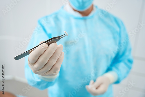 Cropped photo of doctor holds in his hand tweezers and a pellet