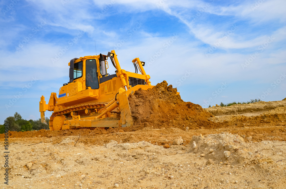 Crawler dozer working on construction site or quarry. Mining machinery moving clay, smoothing gravel surface for new road. Earthmoving, excavations, digging on soils