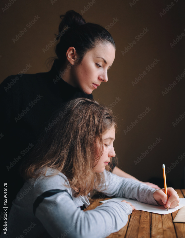 Obraz premium A young ukranian mother helps her daughter write a letter or do her homework. The concept of school lessons, learning and distance education.