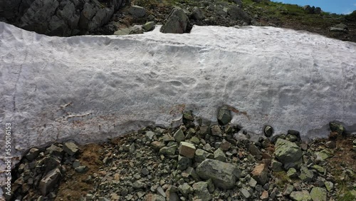 Aerial video of mount Sarlyk slopes. Drone flies backwards along slope with snowfield and rocks. Altai highlands. photo