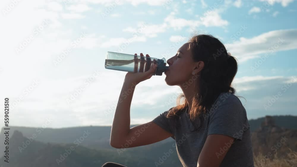 a girl sits on a red cured blanket in nature during sunset with a dog and drinks water from a reusable bottle