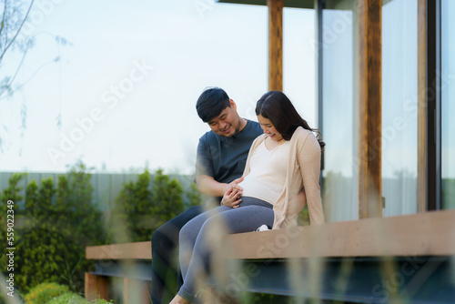 Asian pregnant woman with her husband talking together in terrace at home for relax and breath of fresh air.