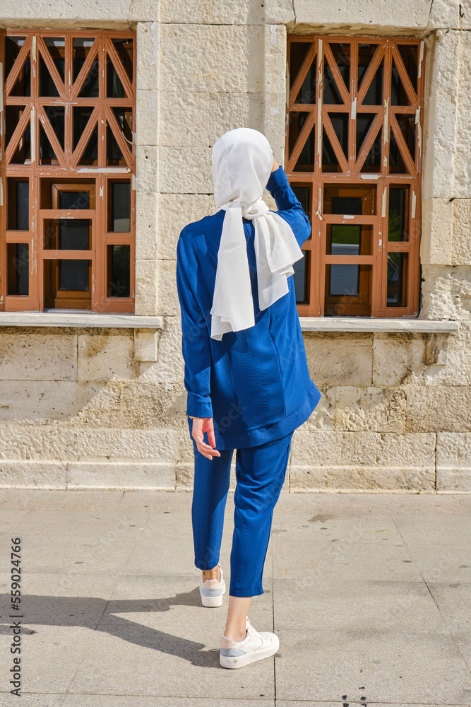 Portrait of Veiled Muslim woman walking in public garden on back view. Young girl in traditional muslim blue clothes on a background of green grass. Stands with your back.