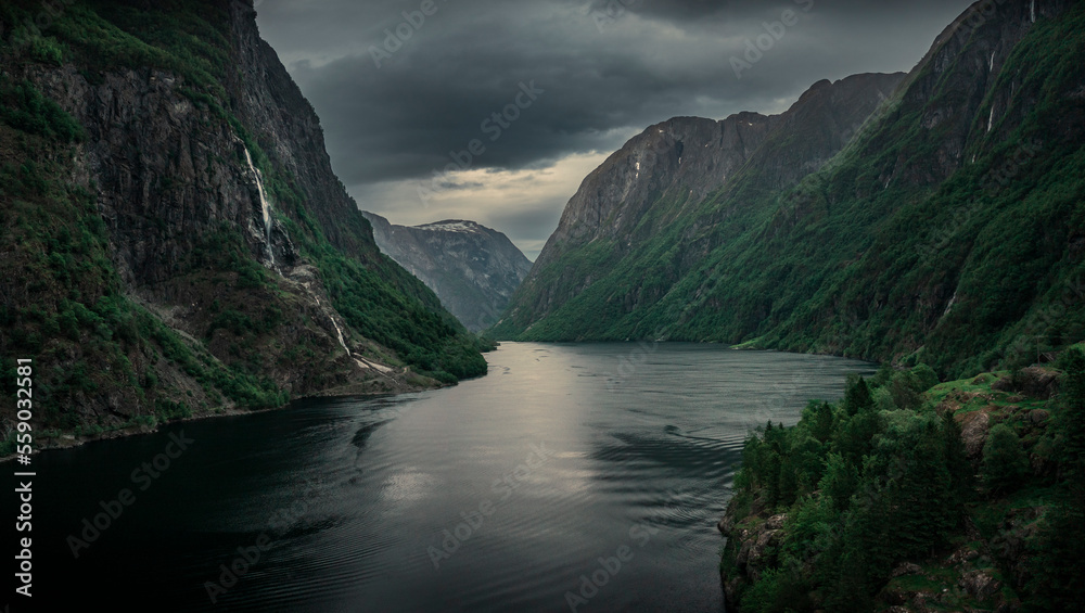 Moody fjord with mountains and waterfall of Aurlandsfjord at Gudvangen in Norway, dark clouds in the sky, from above