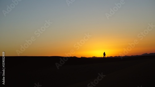 A lone man walking on the edge of a sand dune belonging to a moroccan Sahara erg at sunset, near the settlement of Merzouga.
