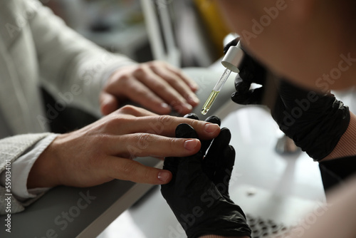 Professional manicurist pouring oil on client s nails in beauty salon  closeup