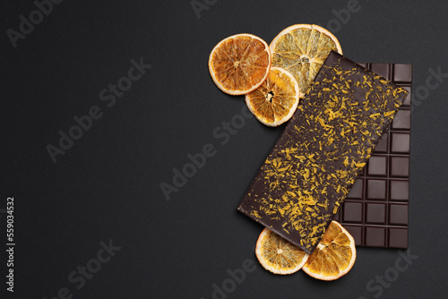 Chocolate bars with freeze dried orange on black background, flat lay. Space for text