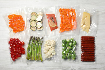 Different food products in vacuum packs on white wooden table, flat lay