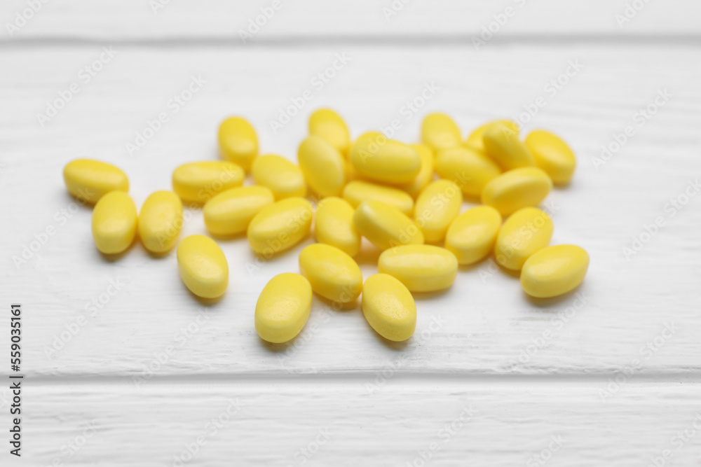 Many yellow dragee candies on white wooden table, closeup