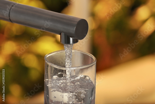 Filling glass with tap water from faucet on blurred background, closeup. Space for text