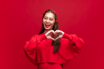 Young asian woman wearing red sweater dress shapes heart gesture on red background for Chinese new year and Christmas festival
