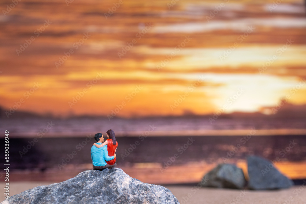 Miniature people , Couple sitting on a sea beach with sunset background