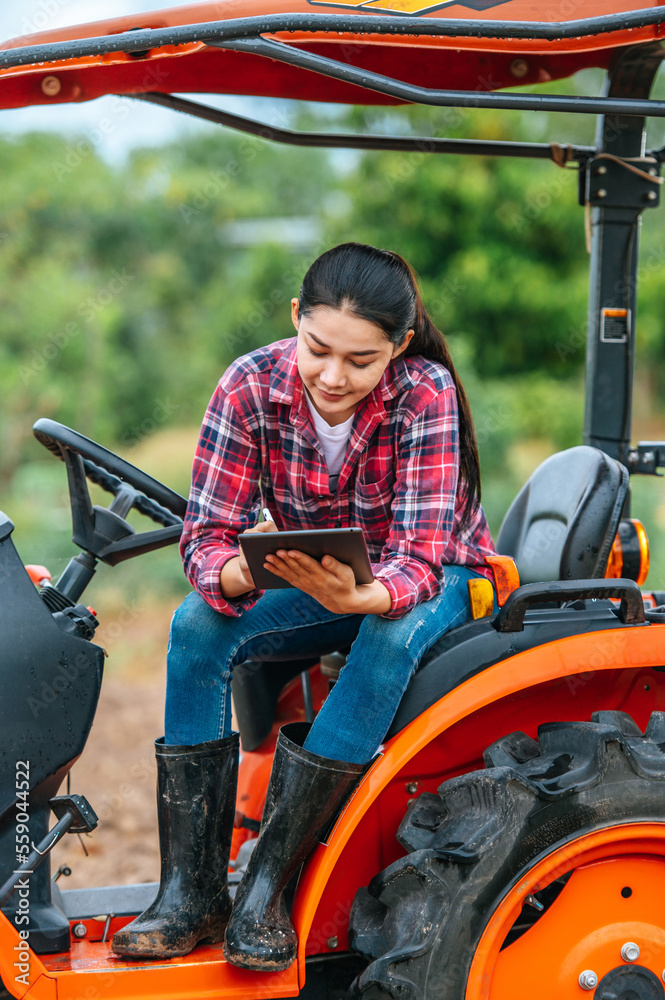 Obraz premium Asian young female farmer sitting on big tractor machine in farmland. Modern technologies in agriculture management and agribusiness concept.