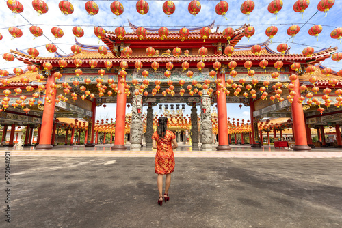 Rear view of Asian woman in red cheongsam qipao dress is visiting the Chinese Buddhist temple during lunar new year for traditional culture concept photo