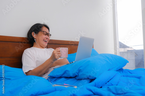 Woman lazing in her bed watching movie on her laptop computer photo