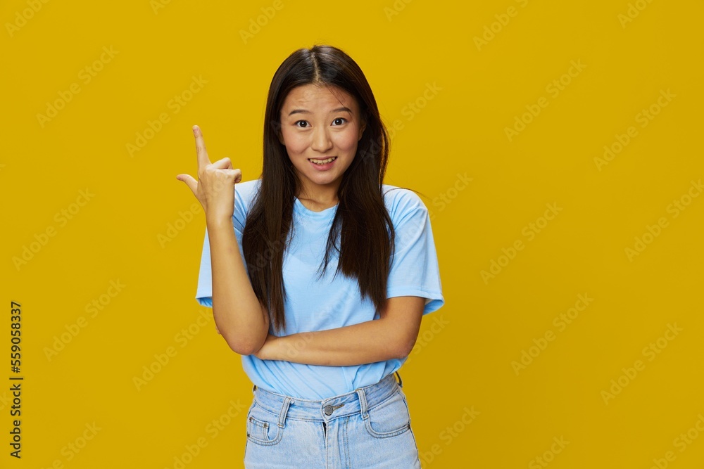 Asian woman smile with teeth hand gestures, signs and symbols on yellow background in blue t-shirt and jeans Asian woman smile with teeth hand gestures, signs and symbols on yellow background in blue t-shirt and jeans