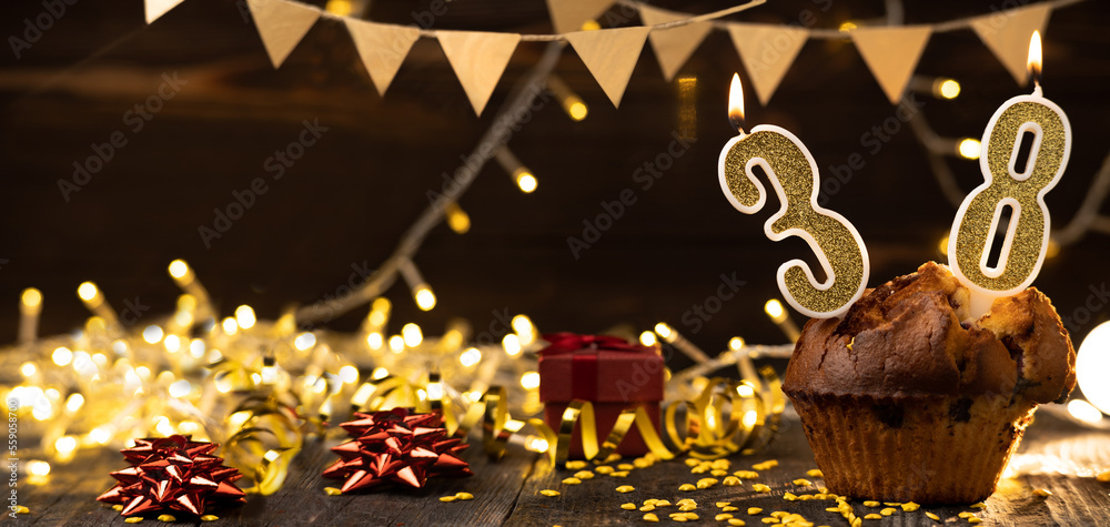Number 38 birthday celebration candle in cupcake against lights and wooden background.