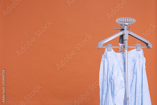 Steamer with a hanger for ironing clothes on a solid color background.