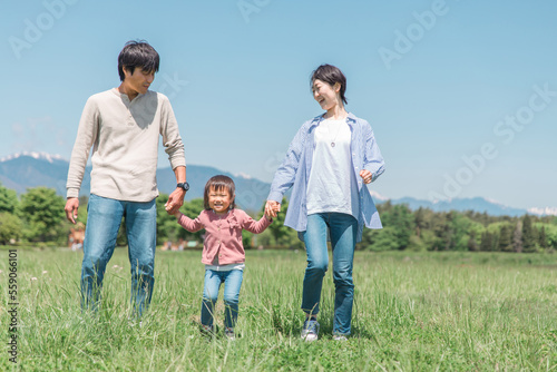 空と高原・草原・公園で手を繋いで歩く子供と両親の家族・ファミリーイメージ 
