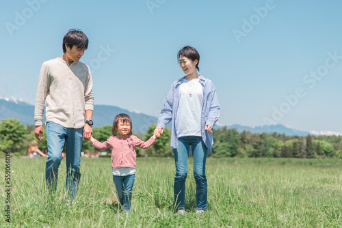 空と高原・草原・公園で手を繋いで歩く子供と両親の家族・ファミリーイメージ  © buritora