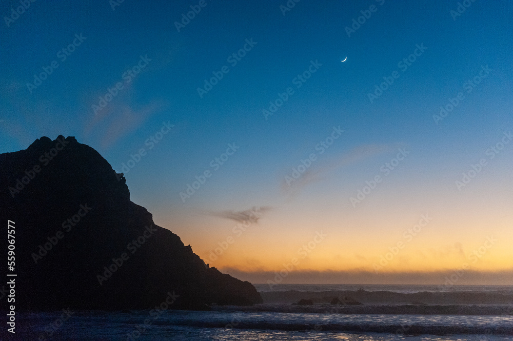 Bright orange sky at Pfeiffer beach, around sunset. Small crescent moon is in the background.