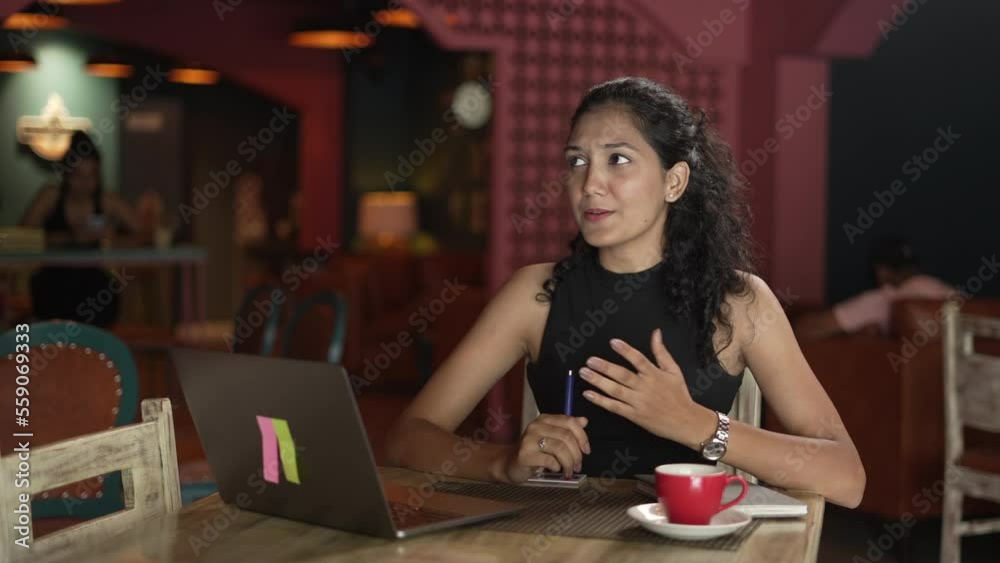 Close-up Portrait of positive Asian business woman doing video call on laptop while drinking coffee.and looking at laptop screen indoors. young Indian business woman siting at table in the restaurant. Close-up Portrait of positive Asian business woman doing video call on laptop while drinking coffee.and looking at laptop screen indoors. young Indian business woman siting at table in the restaurant.