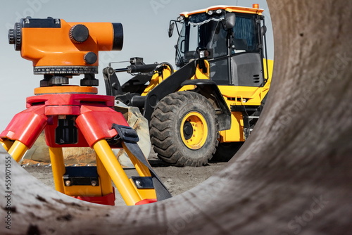 A bulldozer or loader plans the ground at a construction site. View from a large pipe. Close-up of earthmoving equipment. Geodetic equipment - a leveler for accurate work. Modern construction.