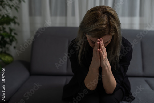 Concentrated brunette woman in t-shirt praying with pray gesture and looking up over white background.