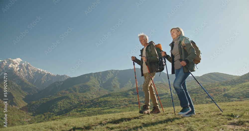 Mature caucasian couple on vacation, having a hike in spring mountains, spending time together after retirement together travelling - tourism, pension concept  - obrazy, fototapety, plakaty 