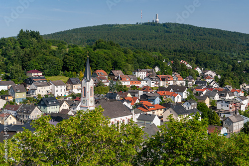 Der Stadtkern der Gemeinde Oberreifenberg im Hochtaunus im Sommer bei schönem Wetter, eingerahmt von Laub- und Nadelbäumen und dem Gipfel des 