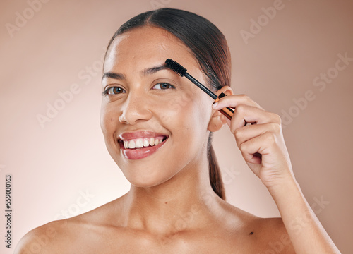 Beauty portrait and eyebrow brush of woman for grooming routine with natural skincare and smile. Young cosmetic girl model with healthy skin brushing facial hair on beige studio background.