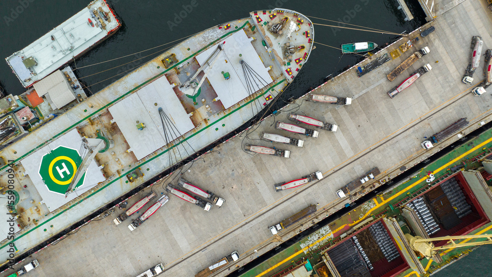 Powder tanker trailer Truck going to load cemant powder to large ship at teminal dock export. powder material transportation by vehicle truck to ship. Corgo container working with crane at dock. Powder tanker trailer Truck going to load cemant powder to large ship at teminal dock export. powder material transportation by vehicle truck to ship. Corgo container working with crane at dock.