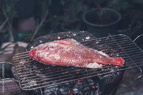 The ruby fish is coated with salt and placed on a charcoal grill in a clay oven.