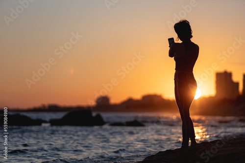 woman making a self portrait at sunset on the beach  selfie with mobile phone  golden sunset  woman with mobile phone