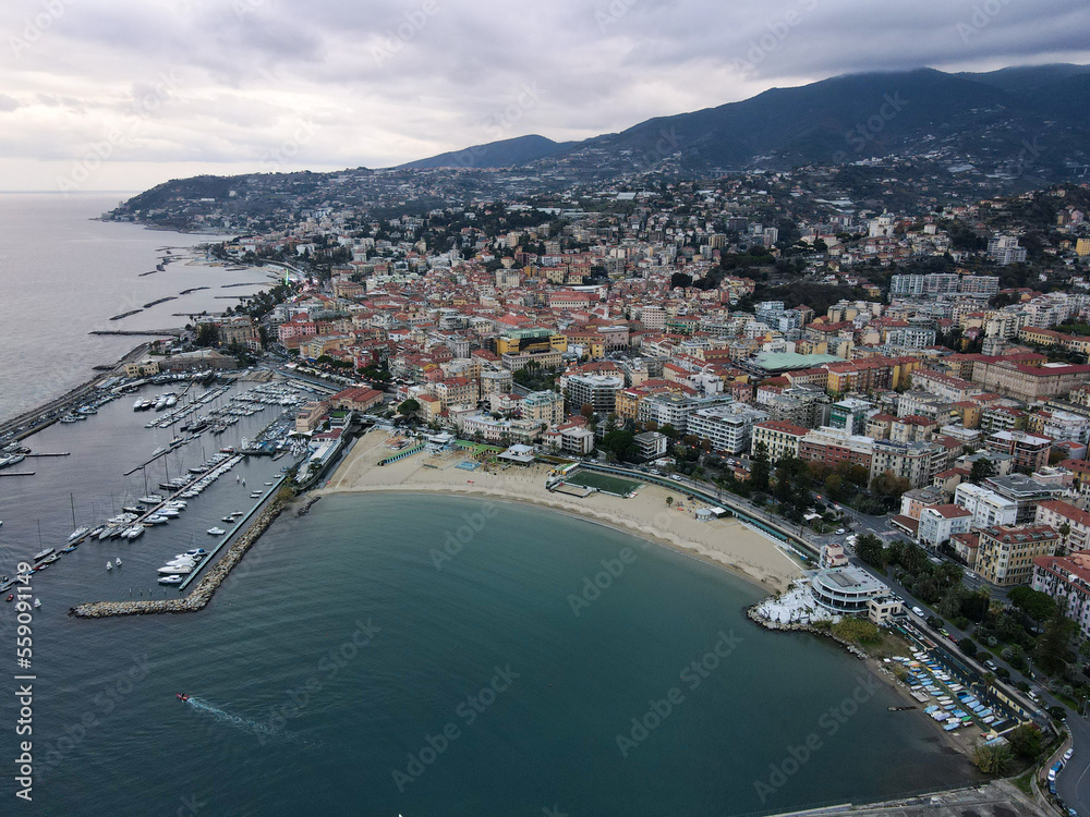 Aerial view of Sanremo, Italian city on the seashore in Liguria, north Italy. Drone flying along the port over beaches and boardwalk with palm trees and Birds Eye of yacht parking in San Remo, Italy.
