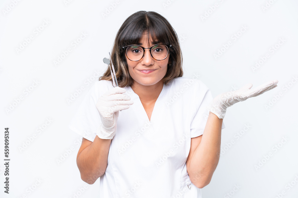 Dentist caucasian woman holding tools isolated on white background having doubts while raising hands Dentist caucasian woman holding tools isolated on white background having doubts while raising hands