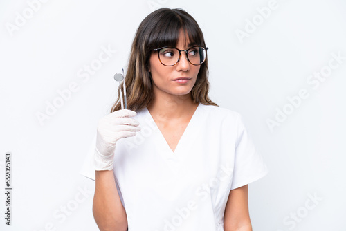 Dentist caucasian woman holding tools isolated on white background looking to the side © luismolinero