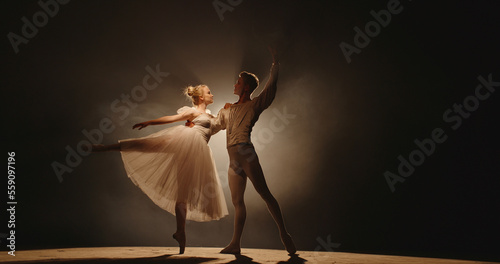 Professional duet of ballet dancers performing on stage isolated on smoked black background. Young choreographers showing their creative art 