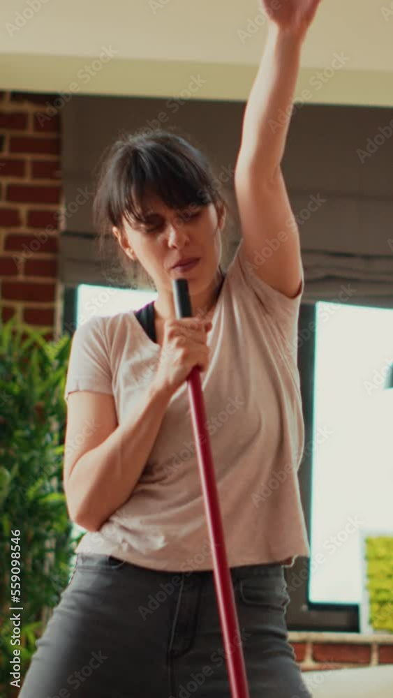 Vertical video: Young woman singing and dancing in living room, washing apartment floors with mop and washing solution. Cheerful housewife mopping tiles and having fun spring cleaning. Handheld shot. Vertical video: Young woman singing and dancing in living room, washing apartment floors with mop and washing solution. Cheerful housewife mopping tiles and having fun spring cleaning. Handheld shot.