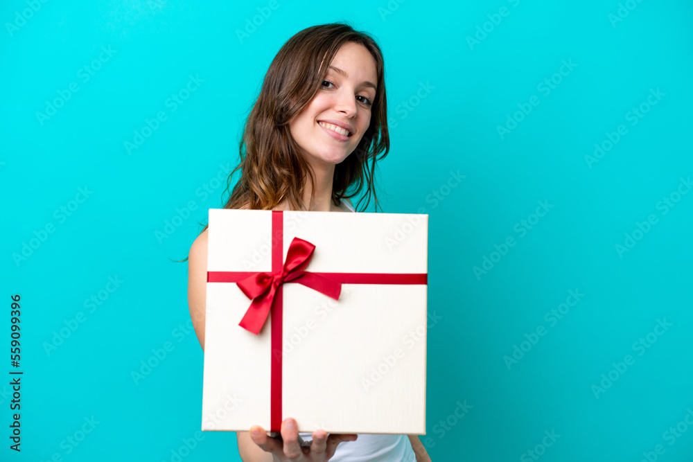 Young caucasian woman holding a gift isolated on blue background with happy expression Young caucasian woman holding a gift isolated on blue background with happy expression