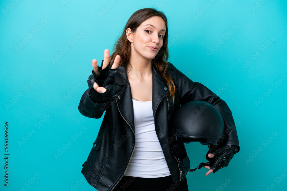 Young caucasian woman with a motorcycle helmet isolated on blue background happy and counting three with fingers