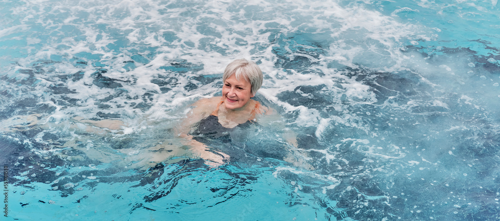 Mature woman swimming in outdoor thermal pool with hydromassage.