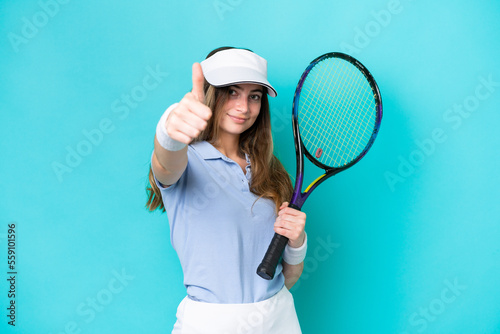 Young tennis player woman isolated on blue background with thumbs up because something good has happened