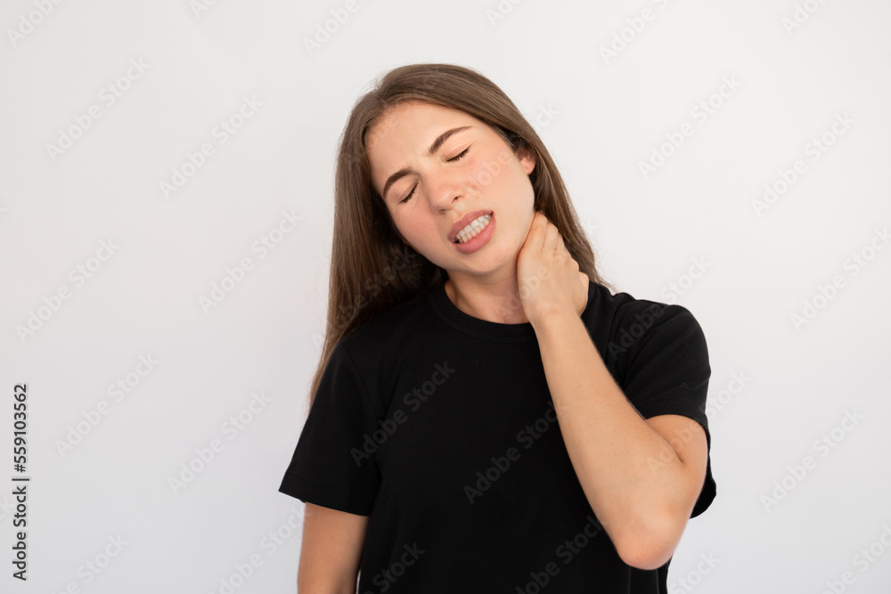 Portrait of tired young woman rubbing tensed neck over white background. Caucasian lady wearing black T-shirt sufferimg from strain. Muscle pain concept Portrait of tired young woman rubbing tensed neck over white background. Caucasian lady wearing black T-shirt sufferimg from strain. Muscle pain concept