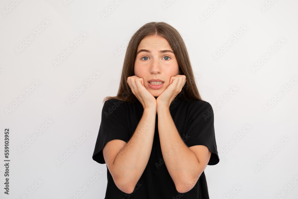 Portrait of scared young woman looking at camera over white background. Caucasian lady wearing black T-shirt touching face with worried expression. Anxiety concept Portrait of scared young woman looking at camera over white background. Caucasian lady wearing black T-shirt touching face with worried expression. Anxiety concept