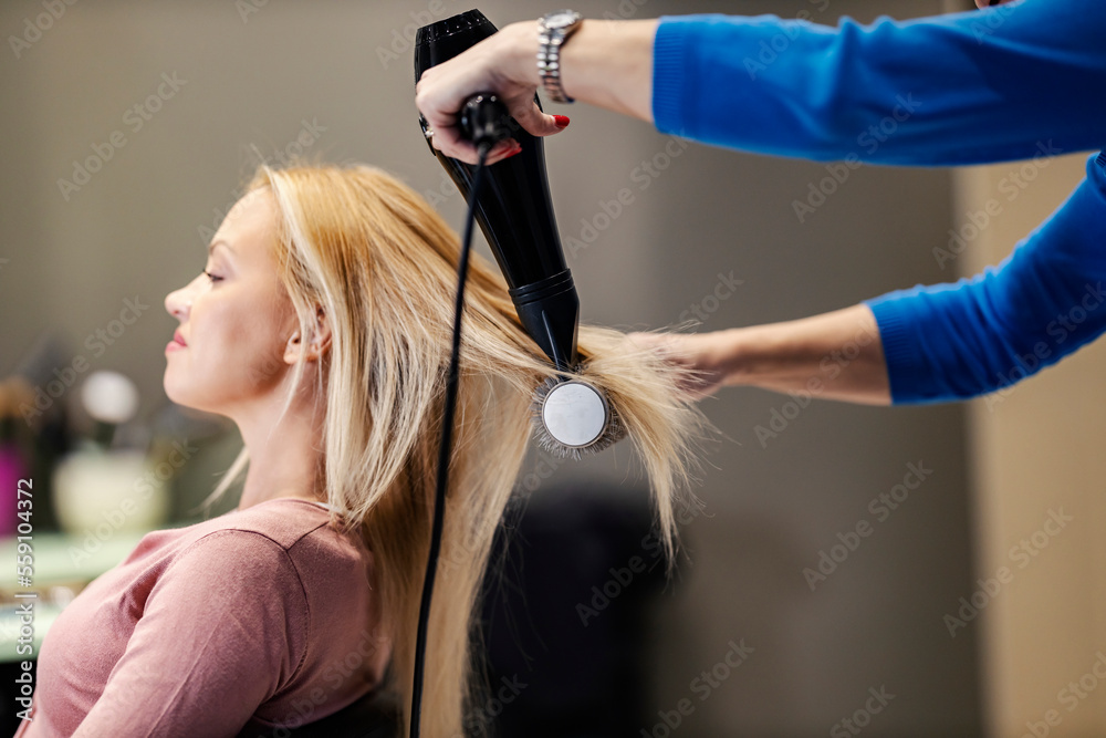 A hair stylist is styling customer's hair with brush and hairdryer. A hair stylist is styling customer's hair with brush and hairdryer.