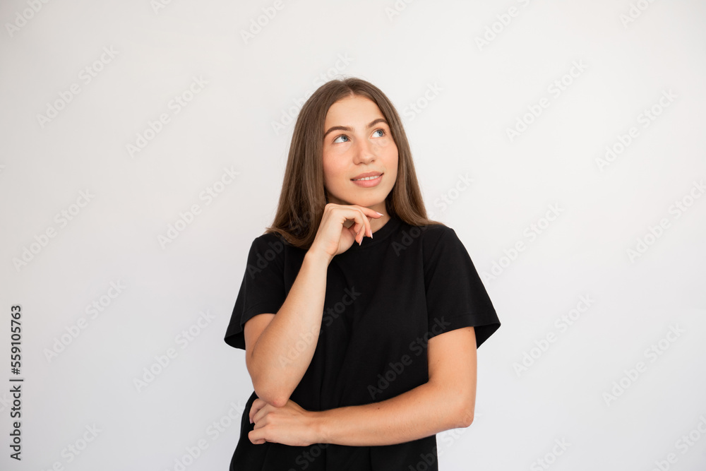 Portrait of thoughtful young woman looking away over white background. Caucasian lady wearing black T-shirt posing with hand on chin and smiling. Thinking and dreaming concept Portrait of thoughtful young woman looking away over white background. Caucasian lady wearing black T-shirt posing with hand on chin and smiling. Thinking and dreaming concept