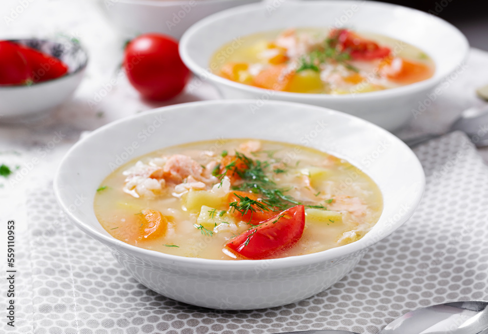 Fish soup with salmon, vegetables and rice in white bowl.